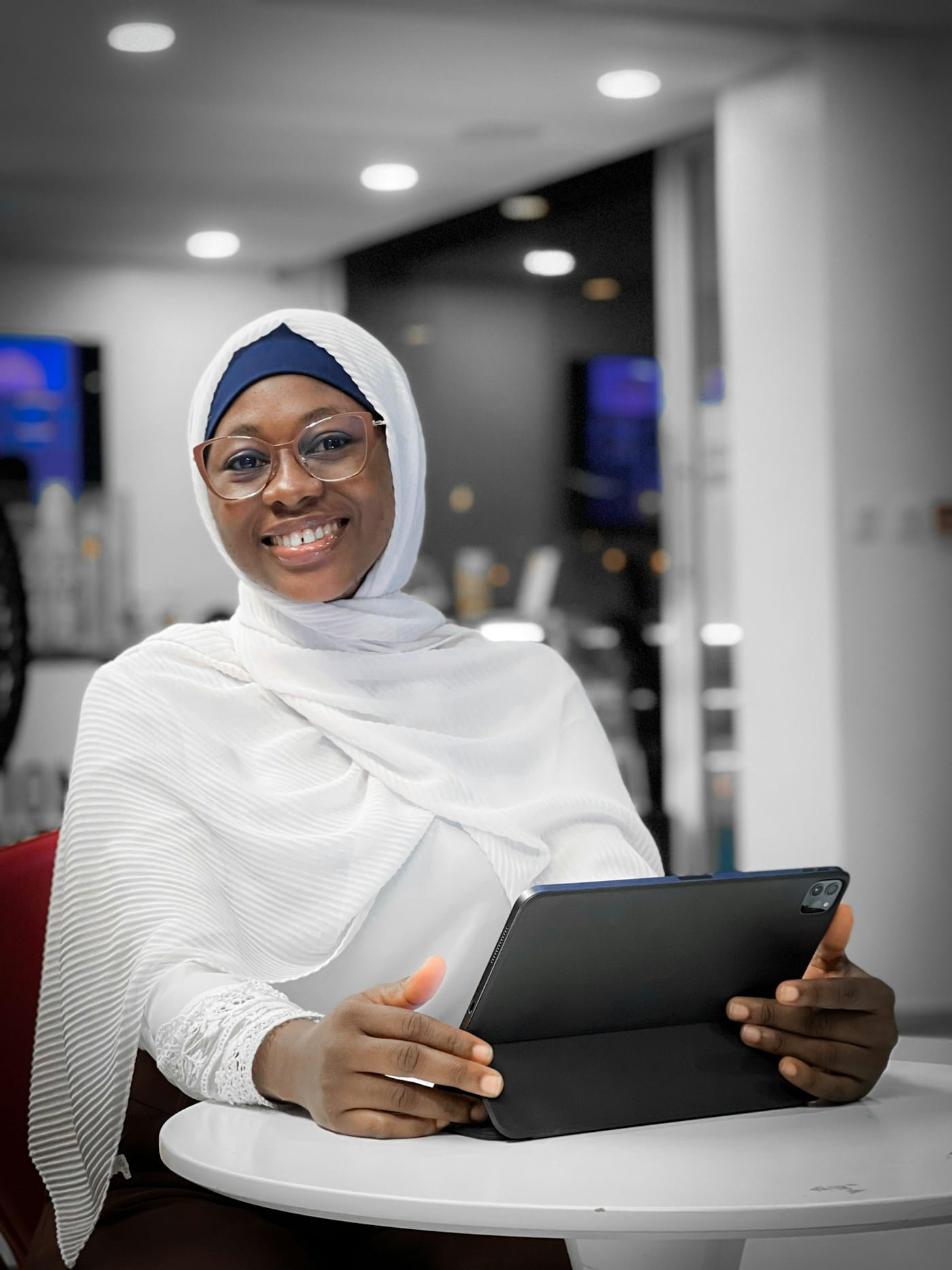 A woman in a headscarf smiling with a tablet at a table