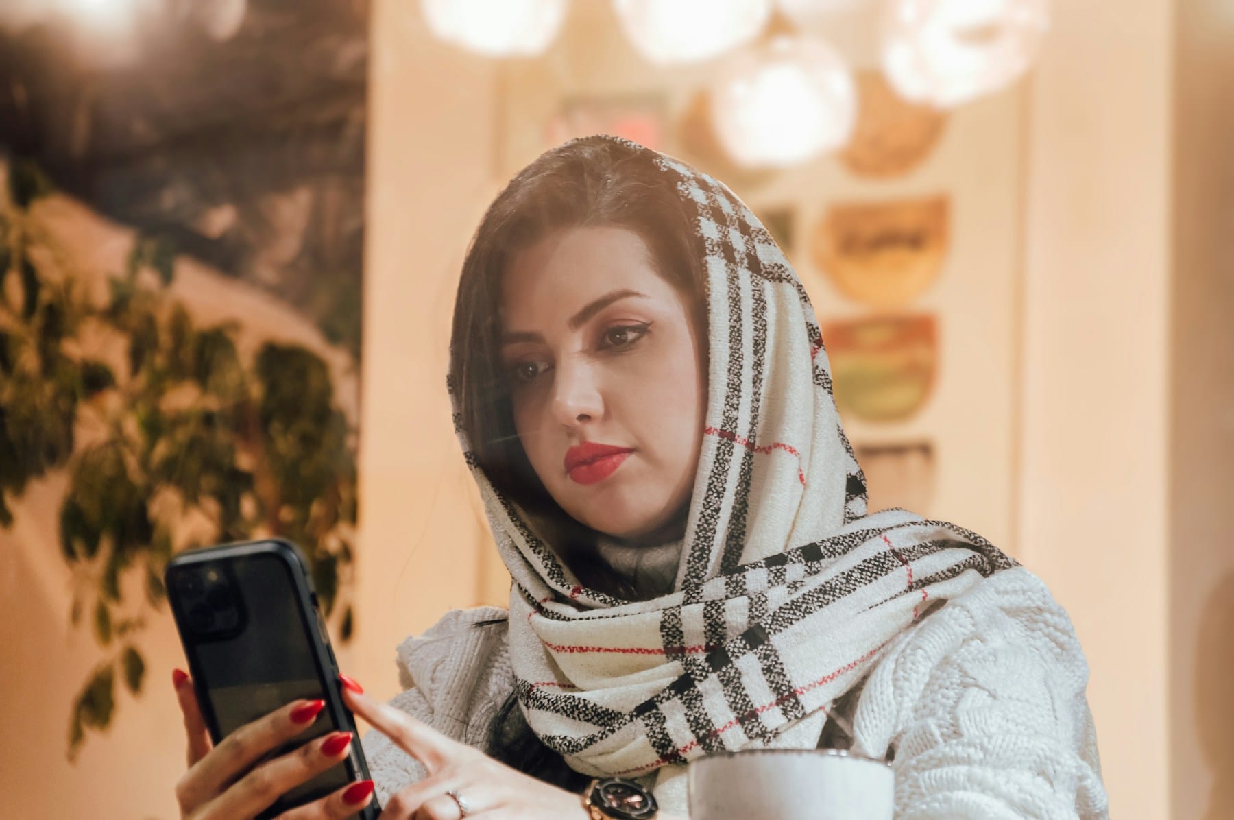 A young woman in a headscarf reading her phone in a café